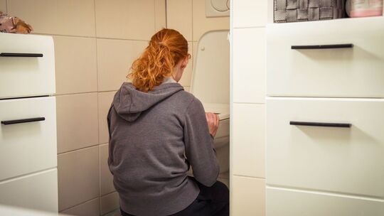 Frau hockt vor einer Toilette im Badezimmer