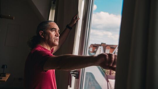 Mann steht vor dem Fenster seiner Wohnung