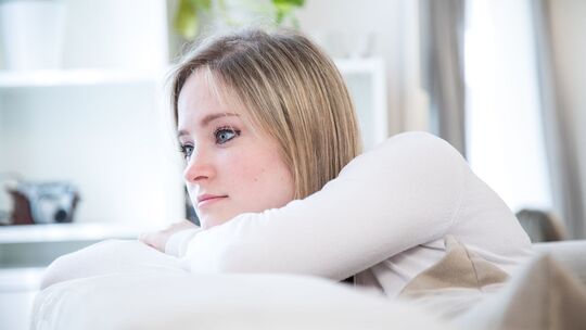Eine junge Frau lehnt nachdenklich auf dem Sofa