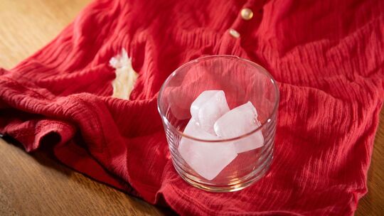 Glas mit Eiswürfeln steht auf einem Shirt mit Kaugummi-Fleck Glas mit Eiswürfeln steht auf einem Shirt mit Kaugummi-Fleck