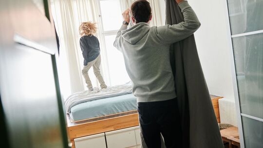 Ein Mann bezieht ein Bett während ein Kind auf dem Bett hüpft