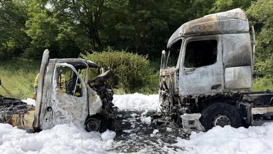 Inmitten von Löschschaum stehen die beiden ausgebrannten Unfallfahrzeuge.