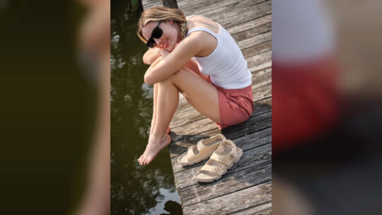 Ein Frau sitzt auf einem Steg neben Sandalen Ein Frau sitzt auf einem Steg neben Sandalen