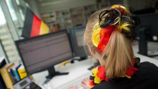 Eine Frau sitzt mit WM-Deko vor einem Computer Eine Frau sitzt mit WM-Deko vor einem Computer
