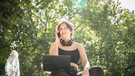 Eine Person mit Laptop und Smartphone im Park Eine Person mit Laptop und Smartphone im Park