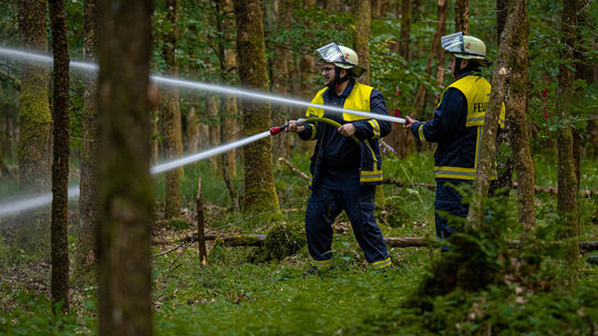 Zwei Einsatzkräfte bekämpfen den angenommenen Vegetationsbrand mit einem Löschangriff im Wald.