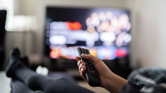 Eine Frau sitzt vor dem Fernseher und hält die Fernbedienung Eine Frau sitzt vor dem Fernseher und hält die Fernbedienung