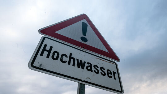 Ein Schild warnt vor Hochwasser, während der Himmel bewölkt ist. Niederschläge und Schneeschmelze haben zahlreiche Pegelstände i