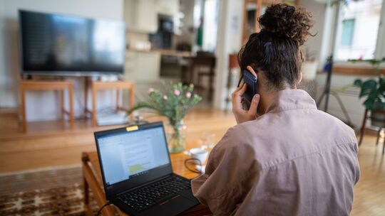Eine Frau telefoniert vor einem geöffneten Laptop zu Hause Eine Frau telefoniert vor einem geöffneten Laptop zu Hause