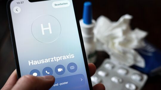 Ein Patient hält ein Smartphone in der Hand und ruft eine Hausarztpraxis an. Geht es nach der Bundesregierung, soll die Möglichk