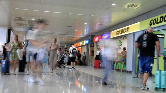 Menschen gehen am Flughafen an Mietwagen-Firmen vorbei