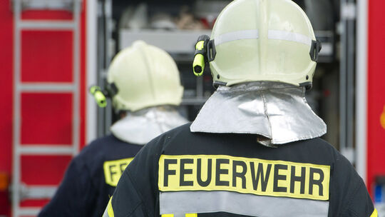 Feuerwehrmänner in Ausrüstung stehen vor einem Einsatzwagen. (Symbolbild)