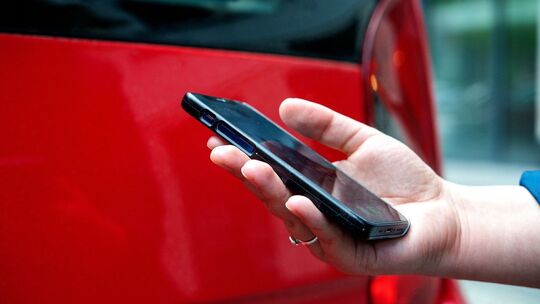 Eine Frau steht mit Smartphone vor einem Auto