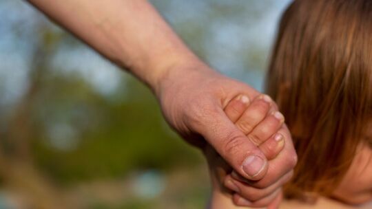 Ein junger Vater hält die Hand seines kleinen Kindes