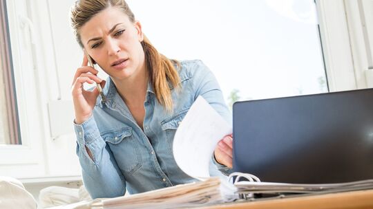 Eine Frau mit Smartphone und Laptop sichtet Unterlagen