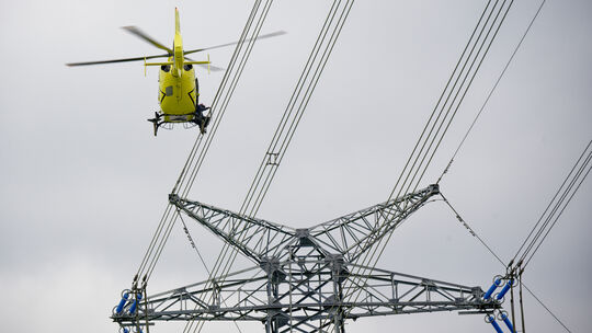 Ein Arbeiter bringt von einem Helikopter aus sogenannte Vogelschutzfahnen an einer neuen Stromleitung des Netzbetreibers Amprion
