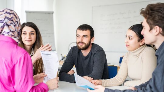Fünf Erwachsene sitzen um einen Tisch in einem Klassenraum Fünf Erwachsene sitzen um einen Tisch in einem Klassenraum