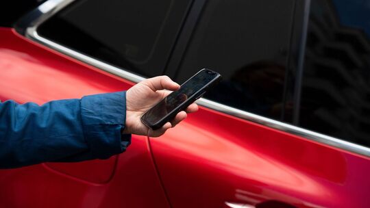 Mann steht mit seinem Smartphone vor einem Auto Mann steht mit seinem Smartphone vor einem Auto