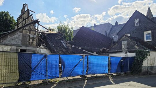 Hinter einem blauen Bauzaun liegen die Reste des vor etwa acht Wochen eingestürzten Hauses.
