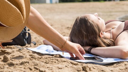 Eine Person stiehlt ein Smartphone am Strand