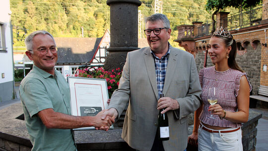 Ortsbürgermeister Achim Reick (links) und Weinhex' Sofie gratulieren Andreas von Canal vom Weingut Freiherr von Heddesdorf zum G