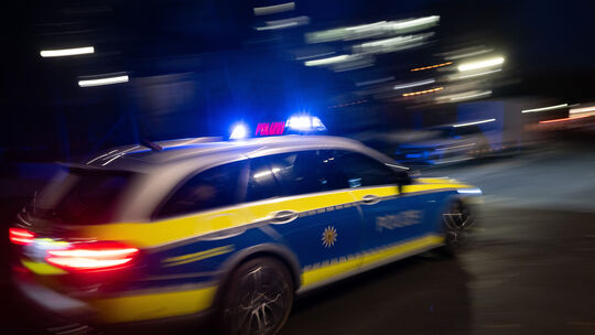 Ein Polizeifahrzeug fährt im Rahmen eines Fototermins mit Blaulicht an einem Gebäude vorbei (Symbolbild).