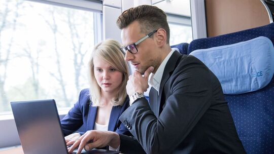 Zwei Personen arbeiten gemeinsam an einem Laptop im Zug