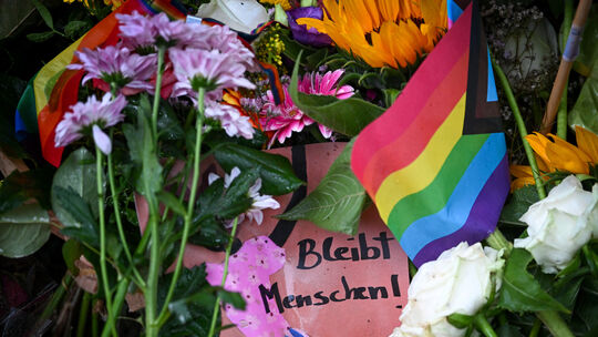 Ein Schild mit der Aufschrift „Bleibt Menschen!“ nahe dem Tatort in Berlin am Fuß eines Baumes, wo ein Fahrzeug am Rande des Chr