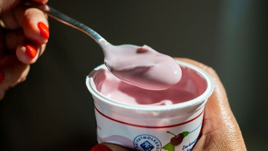Eine Frau öffnet einen Becher Kirschjoghurt