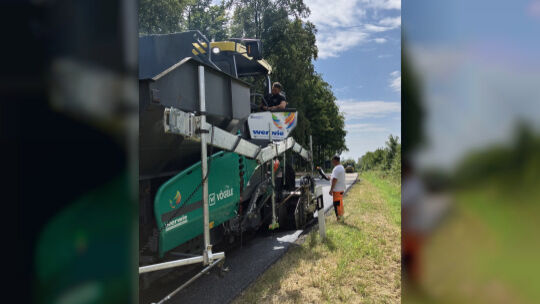 Die Mitarbeiter, die die die Asphaltfertiger bedienen müssen am frischen Asphaltboden, der mit etwa 10 Grad Celsius aus der Masc