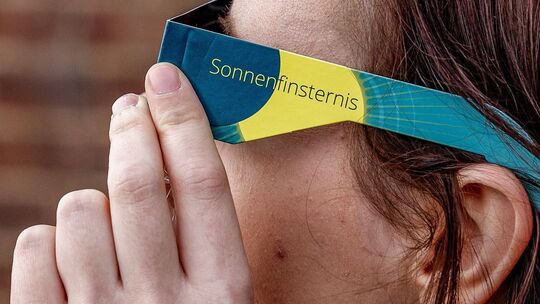 Frau mit Schutzbrille betrachtet eine partielle Sonnenfinsternis
