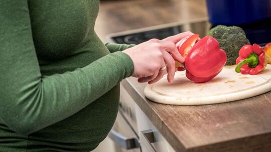 Eine schwangere Frau schneidet sich frisches Gemüse