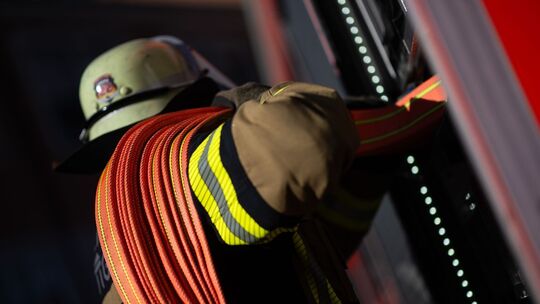 Ein Feuerwehrmann nimmt einen Schlauch aus einem Einsatzfahrzeug der Feuerwehr. (Symbolbild)