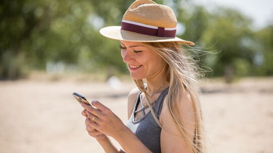 Eine junge Frau nutzt ihr Handy am Strand