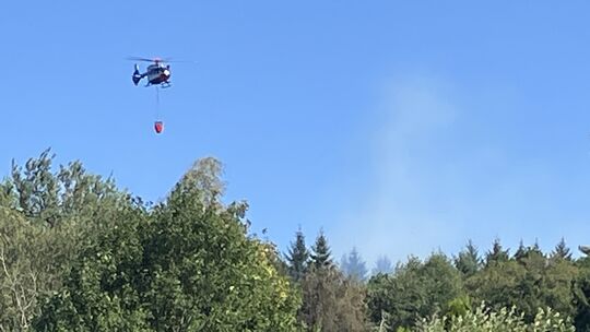 Der mit Wasserbehälter aufgerüstete Polizeihubschrauber fliegt die Brandstelle an.