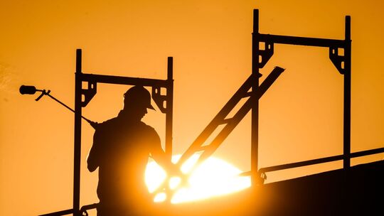 Ein Bauarbeiter im Gegenlicht der Sonne auf einem Gerüst Ein Bauarbeiter im Gegenlicht der Sonne auf einem Gerüst