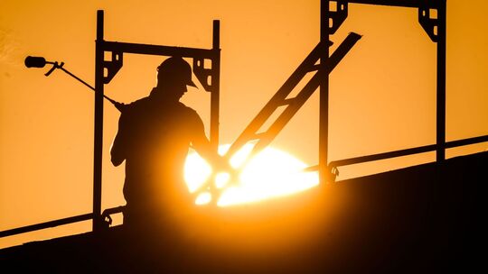 Ein Bauarbeiter im Gegenlicht der Sonne auf einem Gerüst
