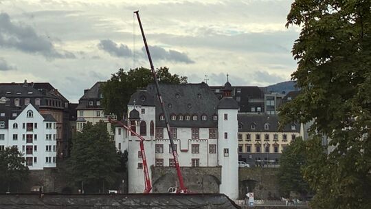 Von der anderen Moselseite kann man beobachten, wie das Dachteil der Alten Burg in der Koblenzer Altstadt am Kran schwebt.
