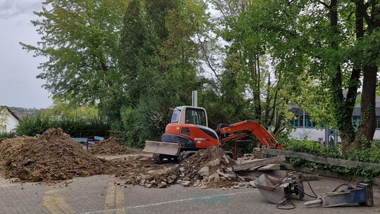 Mithilfe eines Baggers wird der Bereich rund um die kaputte Wasserleitung auf dem Pausenhof der Albert-Schweitzer-Realschule plu
