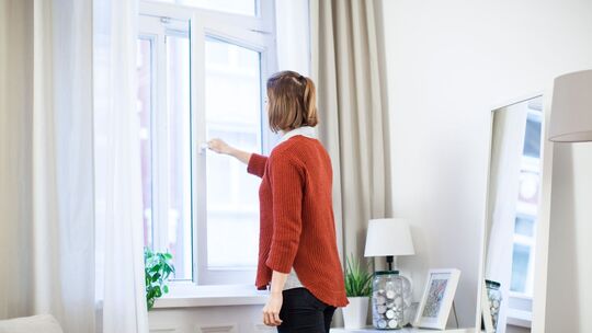 Eine junge Frau öffnet in einer Wohnung das Fenster