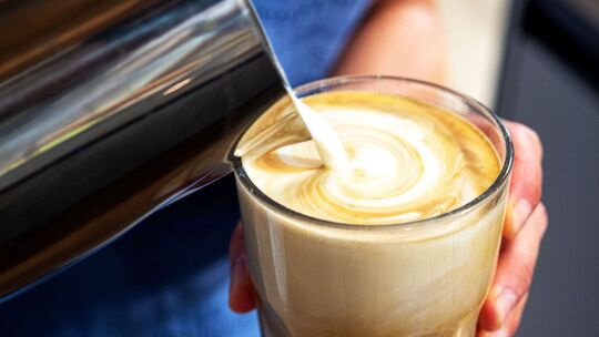Milch wird in einen Kaffee gegossen Milch wird in einen Kaffee gegossen