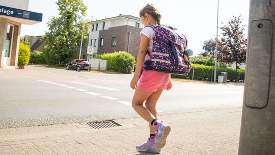 Ein Schulkind läuft mit Rucksack über die Straße