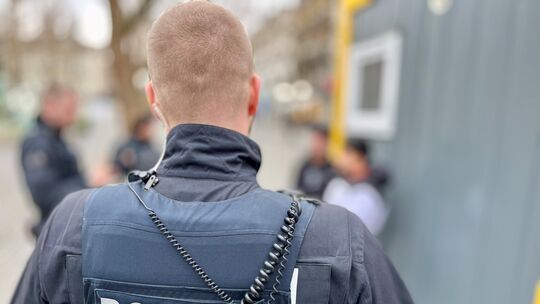 Ein Polizist steht auf dem Neumarkt und beobachtet, wie zwei seiner Kollegen zwei Jugendliche kontrollieren.