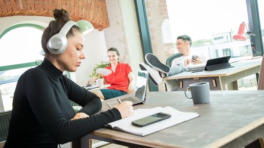 Frau sitzt mit Kopfhörern im Büro Frau sitzt mit Kopfhörern im Büro