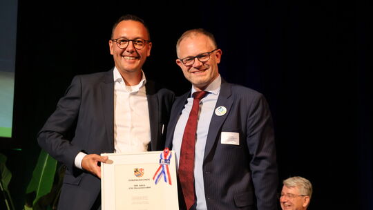 Oberbürgermeister Jan Einig (rechts) überreicht GSG-Geschäftsführer David Meurer eine Ehrenurkunde zum 100. Geburtstag der GSG.