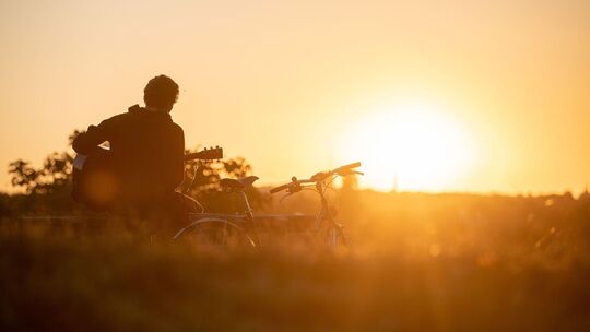Mann spielt im Licht der aufgehenden Morgensonne Gitarre