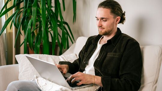 Ein junger Mann nutzt einen Laptop auf dem Sofa Ein junger Mann nutzt einen Laptop auf dem Sofa