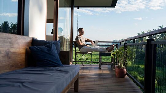 Mann arbeitet auf einem Balkon an einem Laptop Mann arbeitet auf einem Balkon an einem Laptop