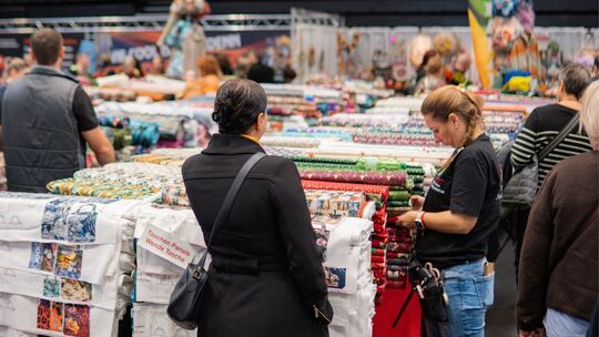 Mehrere Personen stehen an einem langen Tisch, auf dem viele unterschiedliche Stoffe liegen.