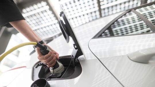 Frau steckt einen Ladestecker für ein E-Auto in eine Buchse